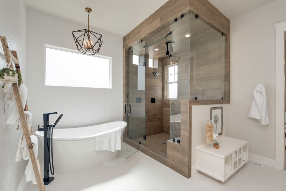 Пример оригинального дизайна: большая главная ванная комната в стиле кантри с плоскими фасадами, светлыми деревянными фасадами, отдельно стоящей ванной, угловым душем, коричневой плиткой, керамогранитной плиткой, серыми стенами, полом из керамогранита, врезной раковиной, столешницей из искусственного кварца, белым полом, душем с распашными дверями и белой столешницей