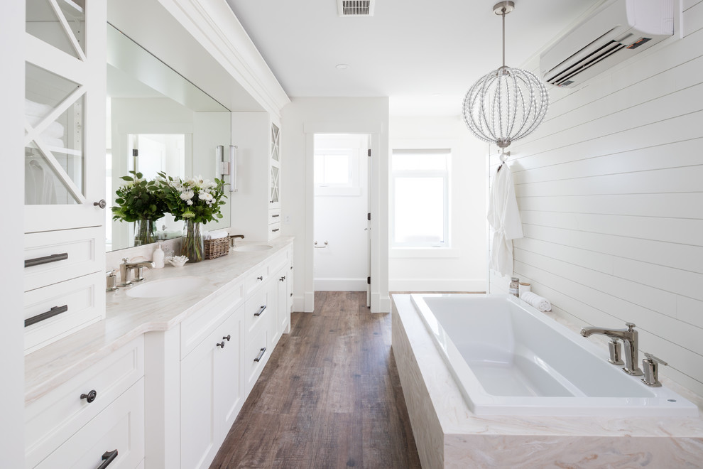 Exemple d'une salle de bain principale nature avec des portes de placard blanches, un plan de toilette en marbre, un plan de toilette blanc, un placard à porte shaker, une baignoire posée, un mur blanc, un sol en bois brun et un sol marron.