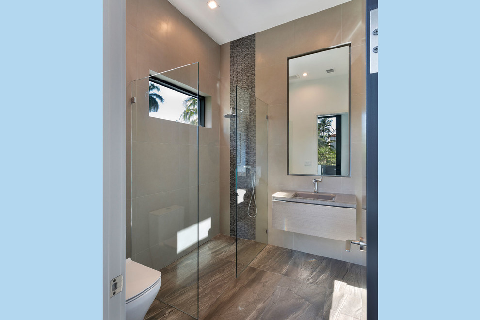 Photo of a medium sized modern ensuite bathroom in Miami with flat-panel cabinets, beige cabinets, a built-in shower, a wall mounted toilet, brown tiles, mosaic tiles, brown walls, lino flooring, an integrated sink, solid surface worktops, beige floors, an open shower and beige worktops.