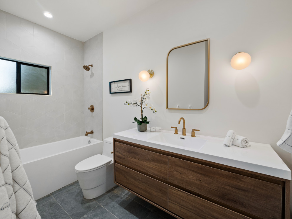 Inspiration för ett funkis vit vitt badrum, med släta luckor, skåp i mörkt trä, ett badkar i en alkov, en dusch/badkar-kombination, grå kakel, vita väggar, ett integrerad handfat och grått golv