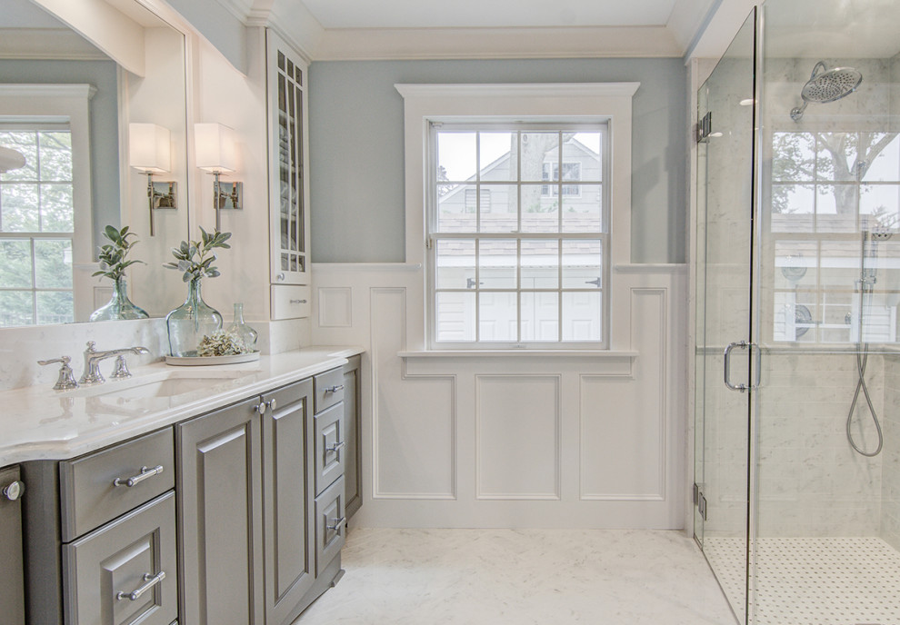 Mid-sized elegant 3/4 white tile and porcelain tile porcelain tile, white floor, single-sink and wainscoting bathroom photo in New York with raised-panel cabinets, gray cabinets, a one-piece toilet, blue walls, an undermount sink, quartz countertops, a hinged shower door, white countertops and a freestanding vanity