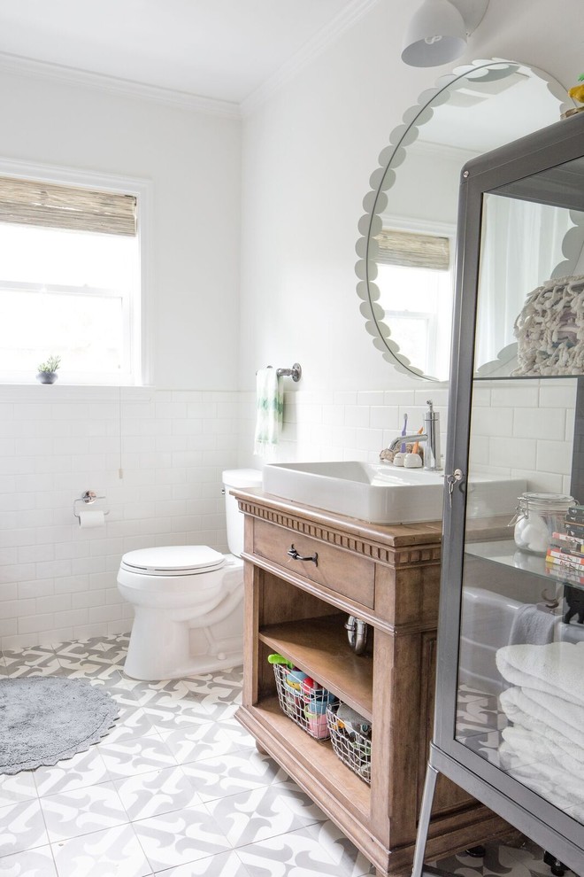 Foto på ett lantligt brun badrum, med skåp i mellenmörkt trä, vit kakel, vita väggar, cementgolv, ett fristående handfat, träbänkskiva, flerfärgat golv och släta luckor