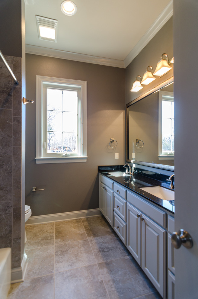 Immagine di una stanza da bagno moderna con lavabo da incasso, ante con bugna sagomata, ante grigie, top in granito, vasca idromassaggio, doccia a filo pavimento e pareti grigie