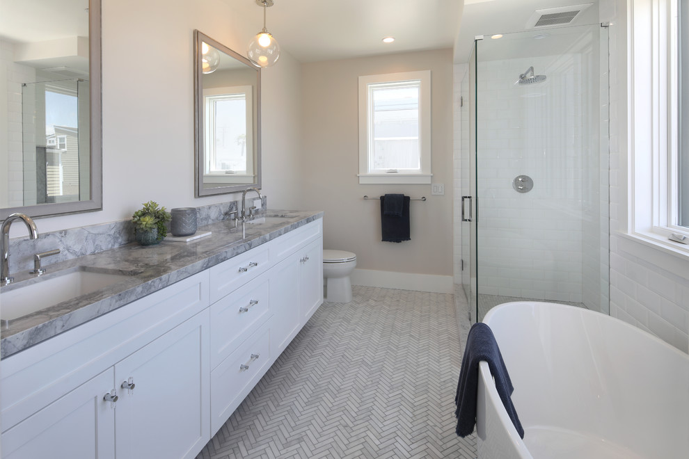 Medium sized beach style ensuite bathroom in Orange County with shaker cabinets, white cabinets, a freestanding bath, a corner shower, white tiles, metro tiles, grey walls, marble flooring, a submerged sink, marble worktops, grey floors, a hinged door and grey worktops.
