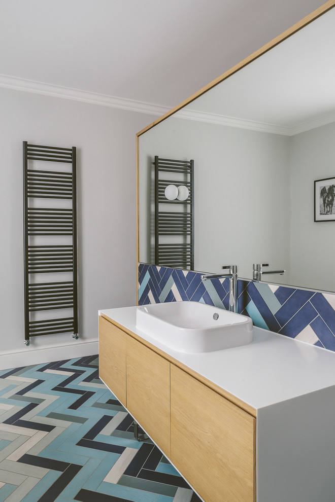 На фото: ванная комната в современном стиле с плоскими фасадами, светлыми деревянными фасадами, разноцветной плиткой, серыми стенами, настольной раковиной, разноцветным полом и белой столешницей с