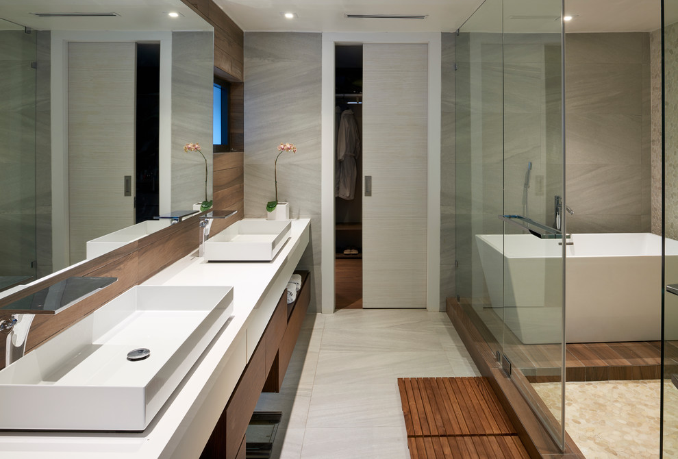 Inspiration for a contemporary ensuite bathroom in Miami with flat-panel cabinets, medium wood cabinets, a freestanding bath, grey tiles, ceramic tiles, grey walls, a vessel sink, engineered stone worktops and a sliding door.