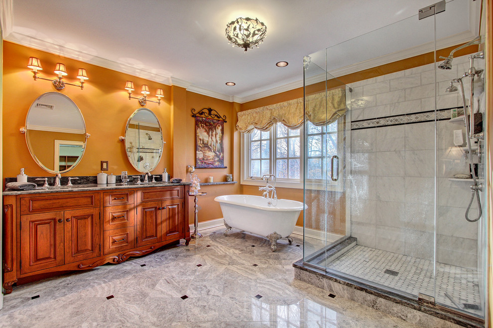 Cette image montre une grande salle de bain principale traditionnelle en bois brun avec un lavabo encastré, un plan de toilette en granite, une baignoire sur pieds, une douche d'angle, un carrelage gris, un carrelage de pierre, un mur marron et un placard avec porte à panneau surélevé.