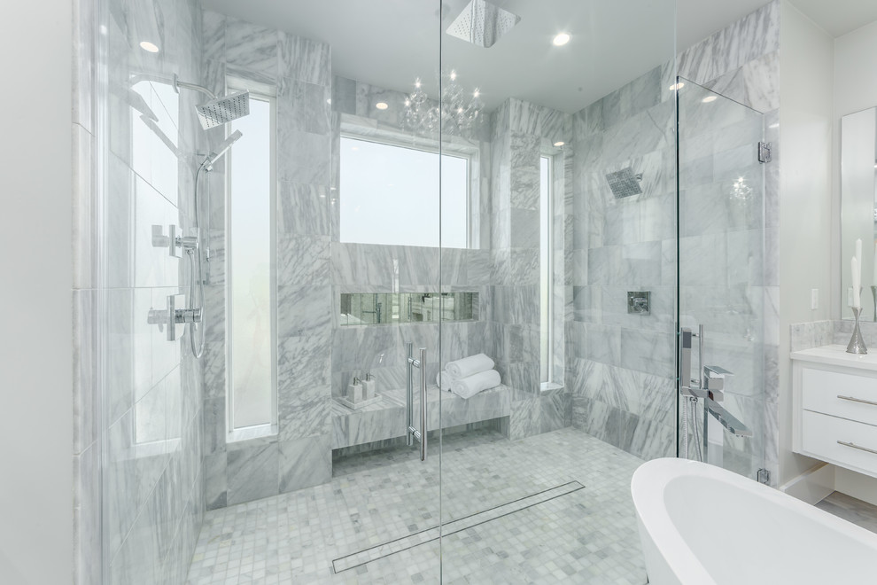 Idéer för att renovera ett mellanstort funkis vit vitt en-suite badrum, med släta luckor, vita skåp, ett fristående badkar, en dubbeldusch, en toalettstol med hel cisternkåpa, vit kakel, stenkakel, vita väggar, marmorgolv, ett integrerad handfat, bänkskiva i kalksten, grått golv och med dusch som är öppen