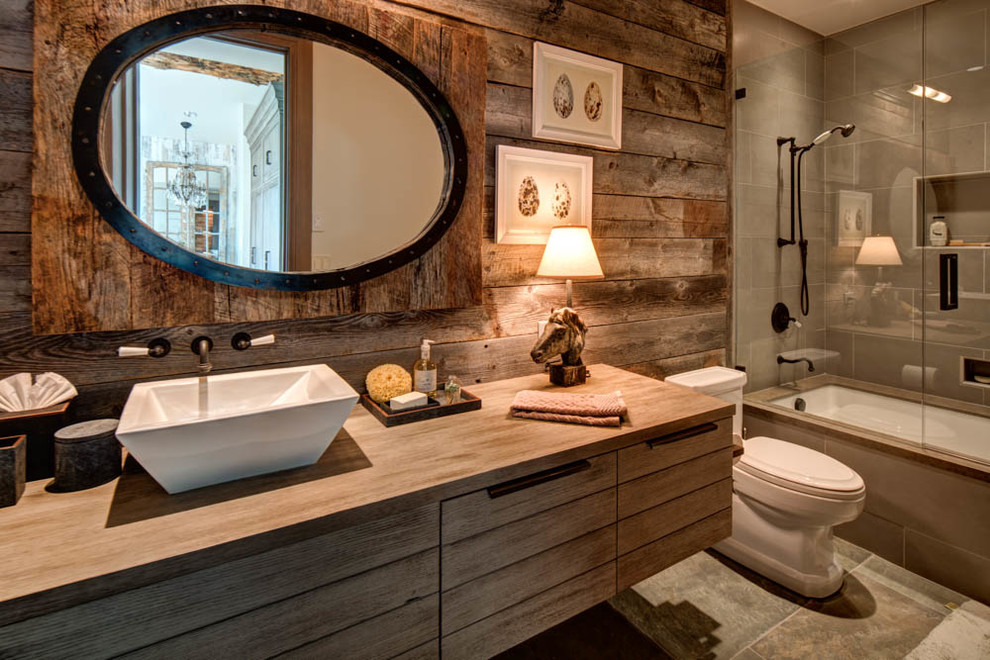 Inspiration pour une salle d'eau chalet en bois brun de taille moyenne avec un combiné douche/baignoire, un carrelage gris, un mur marron, une vasque, une baignoire encastrée, WC à poser, un plan de toilette en bois et un plan de toilette marron.