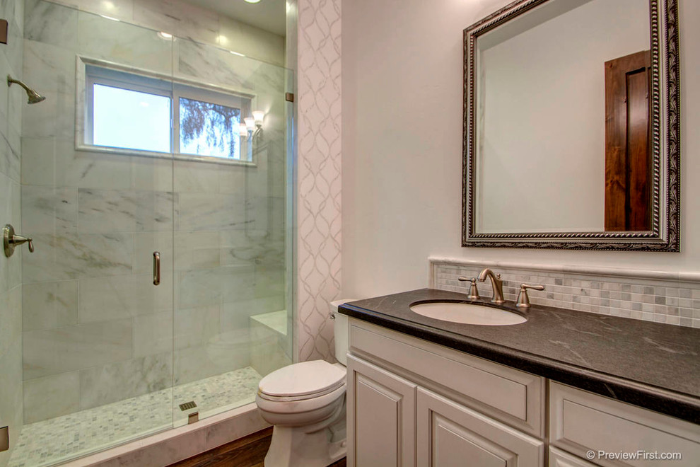 Modelo de cuarto de baño actual con lavabo bajoencimera, puertas de armario blancas, encimera de mármol, baldosas y/o azulejos negros, baldosas y/o azulejos en mosaico, paredes blancas y suelo de baldosas de porcelana