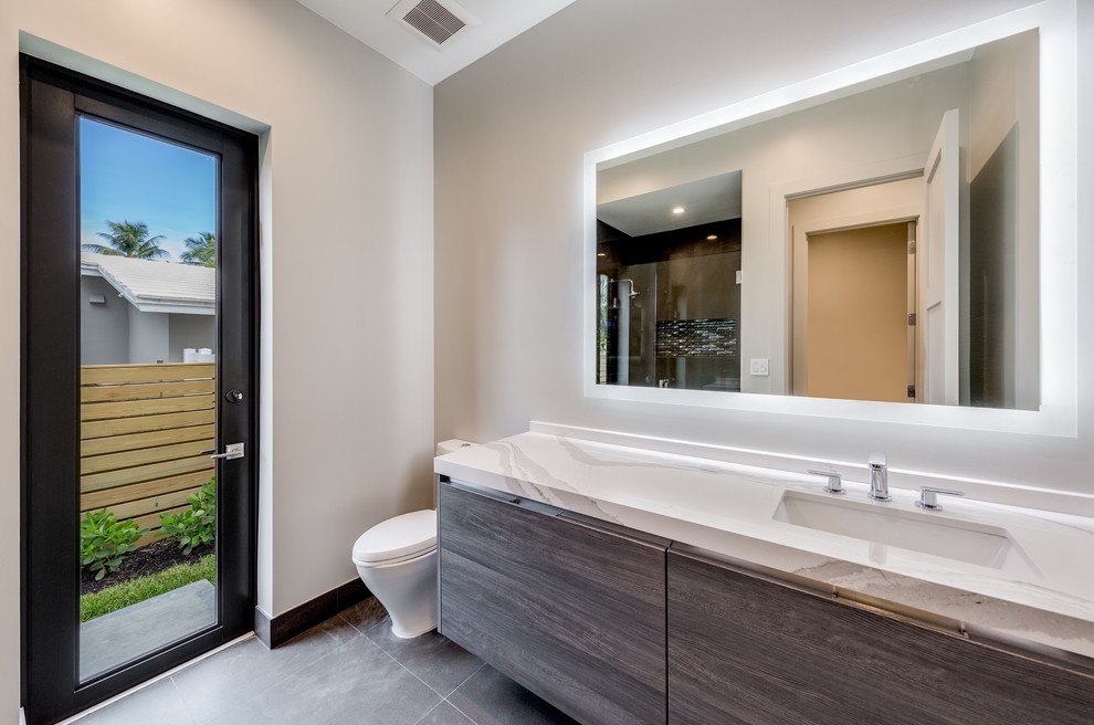 Medium sized traditional ensuite bathroom in Miami with flat-panel cabinets, dark wood cabinets, an alcove shower, a two-piece toilet, beige tiles, beige walls, concrete flooring, a submerged sink, engineered stone worktops, grey floors and a hinged door.