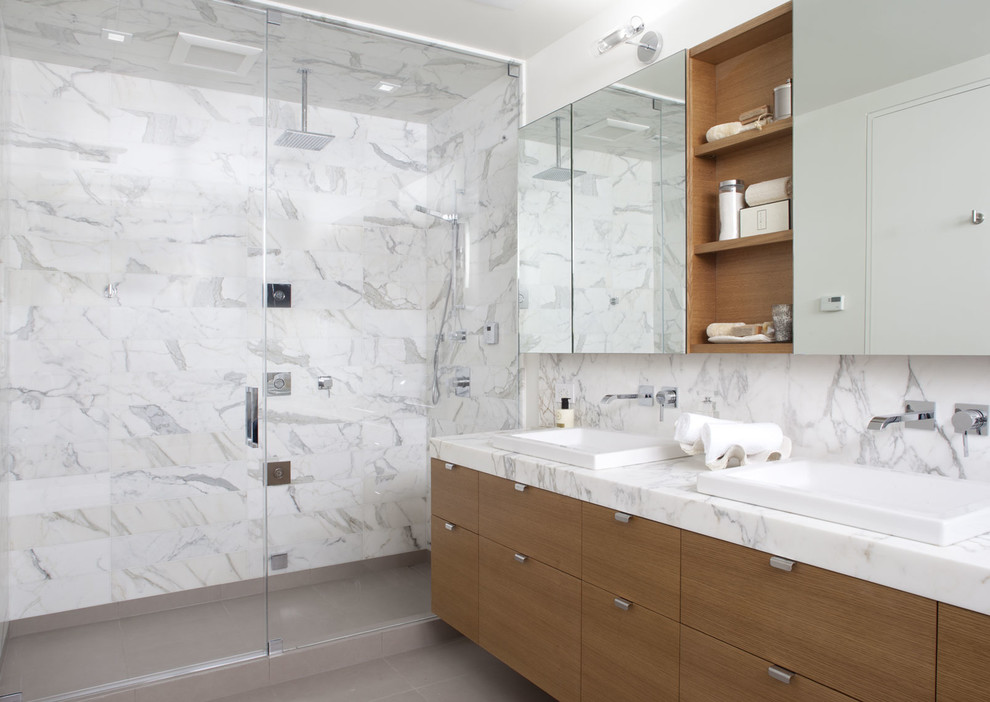 Modern inredning av ett badrum med dusch, med släta luckor, skåp i mellenmörkt trä, en hörndusch, stenkakel, ett nedsänkt handfat, marmorbänkskiva och dusch med gångjärnsdörr