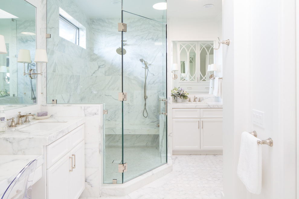 Cette image montre une salle de bain principale traditionnelle avec un placard à porte shaker, des portes de placard blanches, une douche d'angle, du carrelage en marbre, un mur blanc, un sol en marbre, un plan de toilette en marbre et une cabine de douche à porte battante.