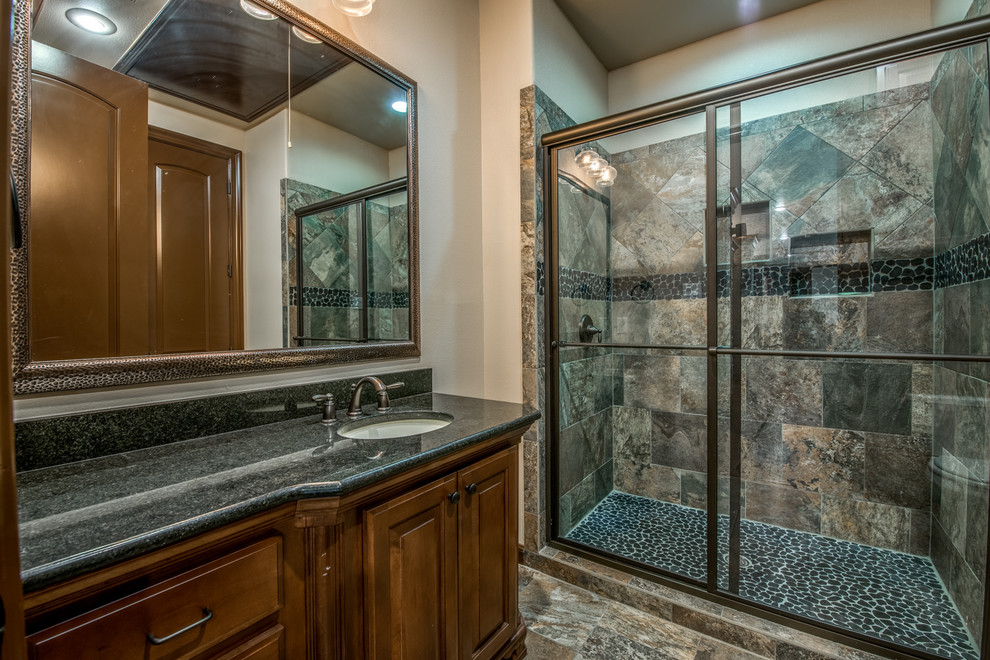 Photo of a medium sized mediterranean shower room bathroom in Austin with raised-panel cabinets, dark wood cabinets, an alcove shower, slate tiles, beige walls, slate flooring, a submerged sink, granite worktops, brown floors and a sliding door.