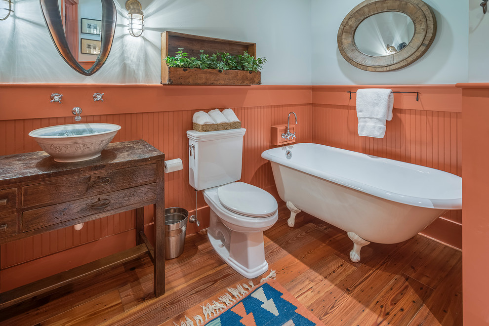 Cette photo montre une salle de bain nature en bois foncé avec une vasque, un placard en trompe-l'oeil, une baignoire sur pieds, WC séparés, un mur orange et un sol en bois brun.