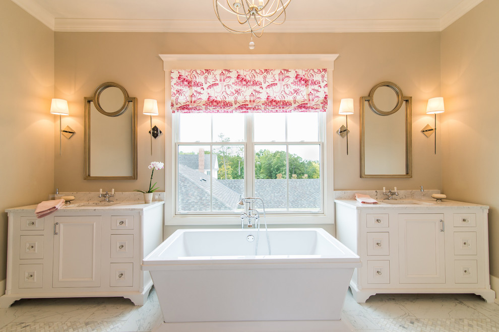 Стильный дизайн: главная ванная комната среднего размера в классическом стиле с белыми фасадами, отдельно стоящей ванной, плиткой из листового камня, мраморным полом, врезной раковиной, мраморной столешницей, бежевыми стенами, зеркалом с подсветкой и фасадами с утопленной филенкой - последний тренд