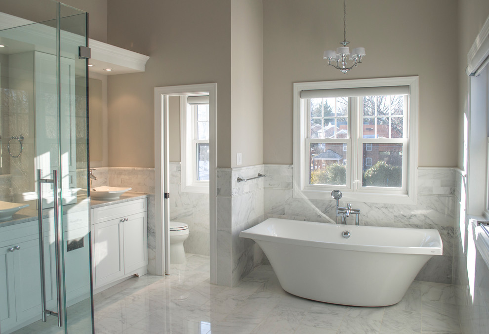 Modelo de cuarto de baño contemporáneo con lavabo sobreencimera, encimera de mármol, bañera exenta, sanitario de una pieza y baldosas y/o azulejos de piedra