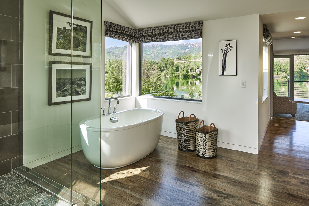 This is an example of a large contemporary ensuite bathroom in Salt Lake City with a freestanding bath, an alcove shower, a one-piece toilet, brown tiles, porcelain tiles, white walls, dark hardwood flooring, brown floors and a hinged door.