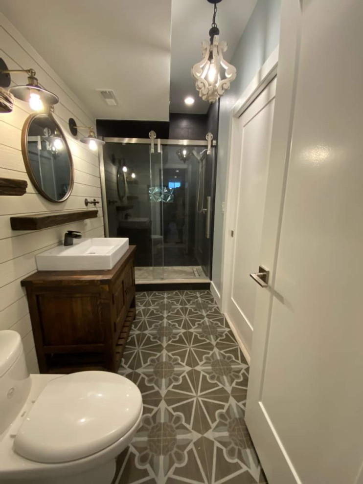 Inspiration for a mid-sized rustic 3/4 black tile and porcelain tile ceramic tile and gray floor sliding shower door remodel in DC Metro with raised-panel cabinets, dark wood cabinets, a one-piece toilet, white walls, a vessel sink, wood countertops and brown countertops