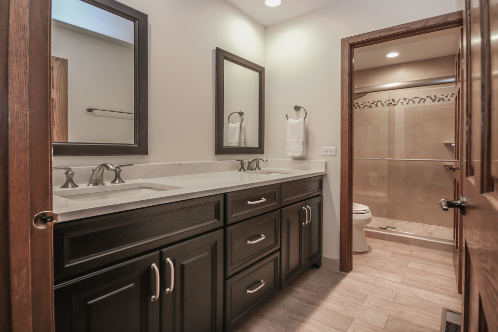 This is an example of a medium sized traditional ensuite bathroom in Chicago with raised-panel cabinets, brown cabinets, an alcove shower, a two-piece toilet, beige tiles, porcelain tiles, beige walls, porcelain flooring, a submerged sink, engineered stone worktops, beige floors, a sliding door and white worktops.