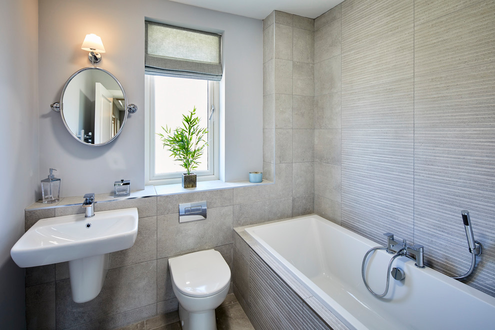 Exempel på ett mellanstort klassiskt badrum för barn, med ett platsbyggt badkar, en toalettstol med hel cisternkåpa, grå kakel, porslinskakel, grå väggar, klinkergolv i porslin, ett väggmonterat handfat och grått golv