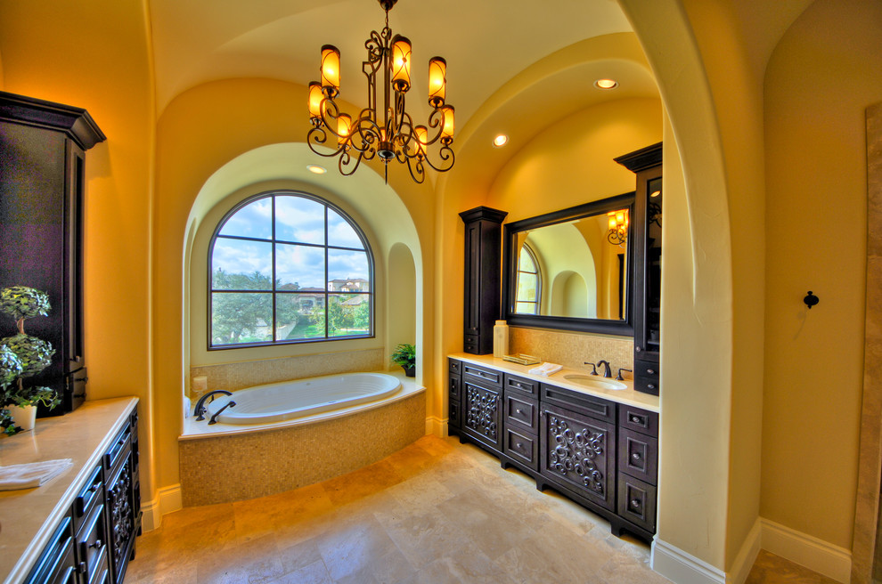 Medelhavsstil inredning av ett stort en-suite badrum, med ett platsbyggt badkar, gula väggar, skåp i mörkt trä, beige kakel, mosaik, kalkstensgolv, ett undermonterad handfat, bänkskiva i kalksten och luckor med infälld panel