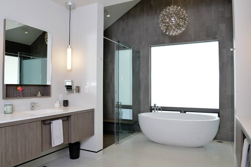 Immagine di una stanza da bagno minimal con lavabo integrato, ante lisce, ante grigie, vasca freestanding, piastrelle grigie, piastrelle in pietra e pareti bianche