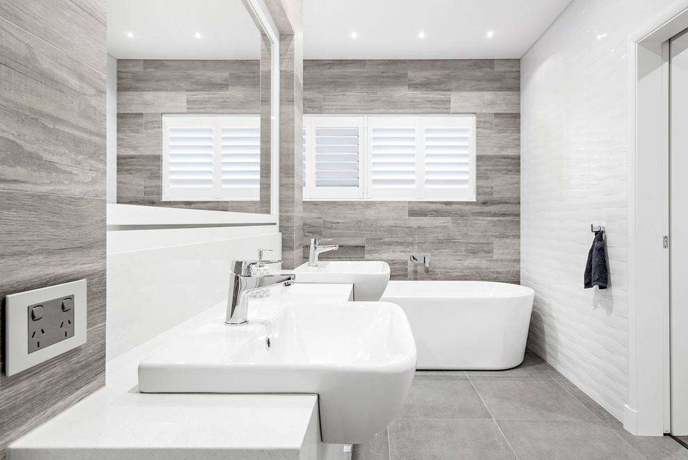 На фото: большая главная ванная комната в стиле модернизм с белыми фасадами, отдельно стоящей ванной, двойным душем, разноцветной плиткой, керамической плиткой, белыми стенами, настольной раковиной, столешницей из искусственного камня, серым полом, открытым душем, белой столешницей и полом из керамической плитки с