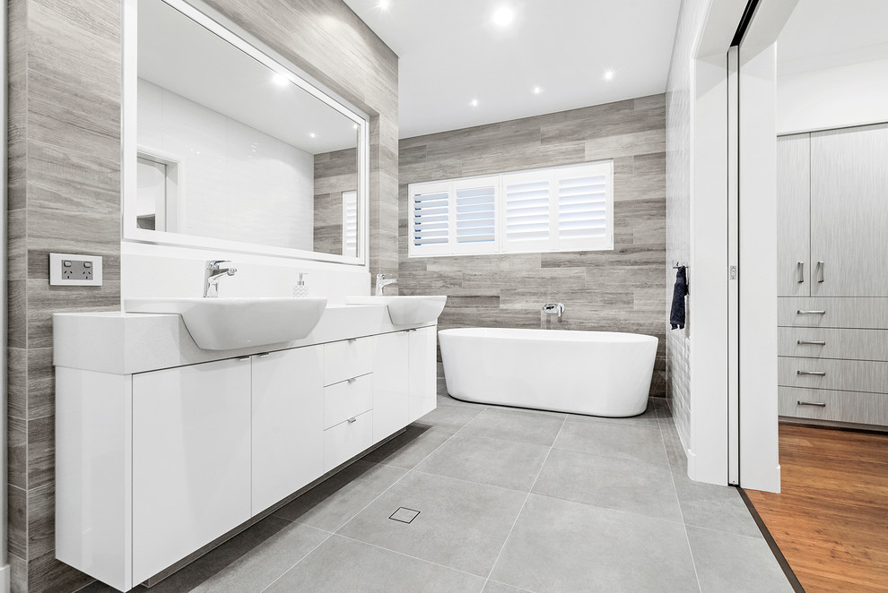 На фото: большая главная ванная комната в стиле модернизм с белыми фасадами, отдельно стоящей ванной, двойным душем, разноцветной плиткой, керамической плиткой, белыми стенами, настольной раковиной, столешницей из искусственного камня, серым полом, открытым душем, белой столешницей и полом из керамической плитки
