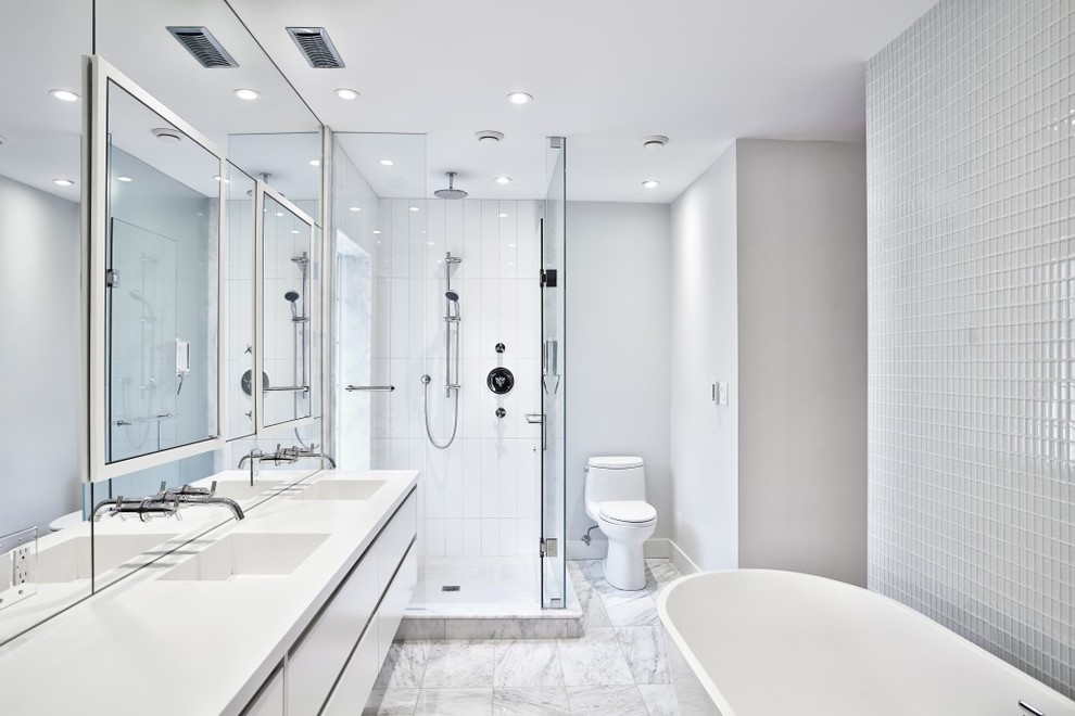 Exempel på ett mellanstort modernt en-suite badrum, med släta luckor, vita skåp, ett fristående badkar, en hörndusch, en toalettstol med separat cisternkåpa, glasskiva, grå väggar, marmorgolv, ett avlångt handfat och bänkskiva i akrylsten