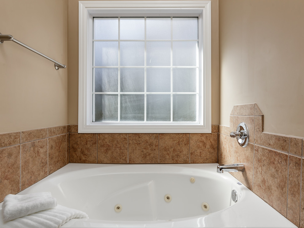 На фото: главная ванная комната среднего размера в стиле кантри с фасадами в стиле шейкер, коричневыми фасадами, гидромассажной ванной, бежевой плиткой, керамической плиткой и столешницей из ламината с