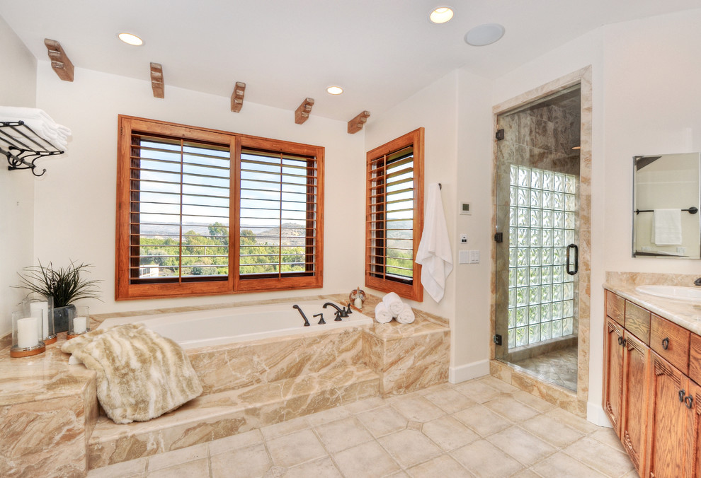 Cette photo montre une grande douche en alcôve principale chic en bois brun avec un placard à porte plane, une baignoire posée, un carrelage beige, un mur beige, un plan vasque et un plan de toilette en granite.