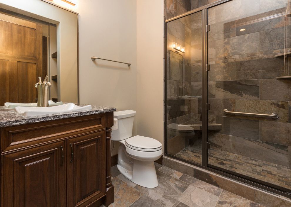 Large 1950s 3/4 gray tile and stone slab slate floor alcove shower photo in Other with a drop-in sink, raised-panel cabinets, dark wood cabinets, granite countertops, a two-piece toilet and white walls