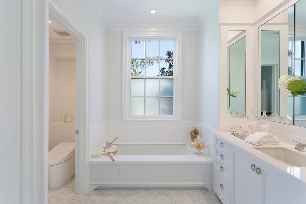 Inspiration for a medium sized traditional ensuite wet room bathroom in Miami with recessed-panel cabinets, white cabinets, an alcove bath, a one-piece toilet, white tiles, porcelain tiles, white walls, marble flooring, a submerged sink, marble worktops, grey floors, a hinged door and grey worktops.