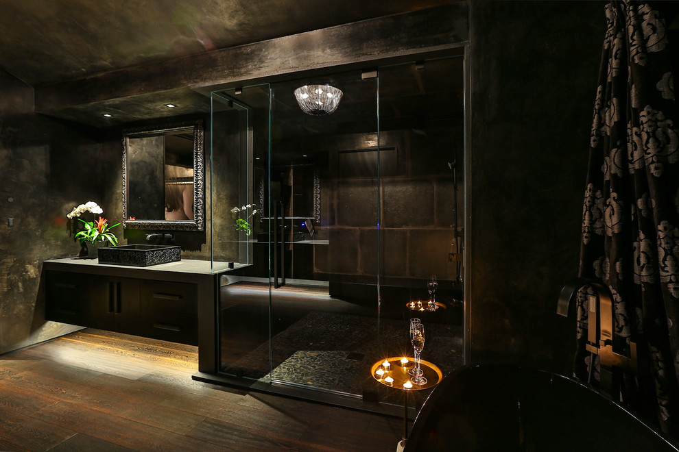 Exempel på ett stort modernt grå grått en-suite badrum, med svarta väggar, mörkt trägolv, släta luckor, skåp i mörkt trä, ett fristående badkar, en öppen dusch, grå kakel, stenkakel, ett avlångt handfat, bänkskiva i betong, brunt golv och dusch med gångjärnsdörr