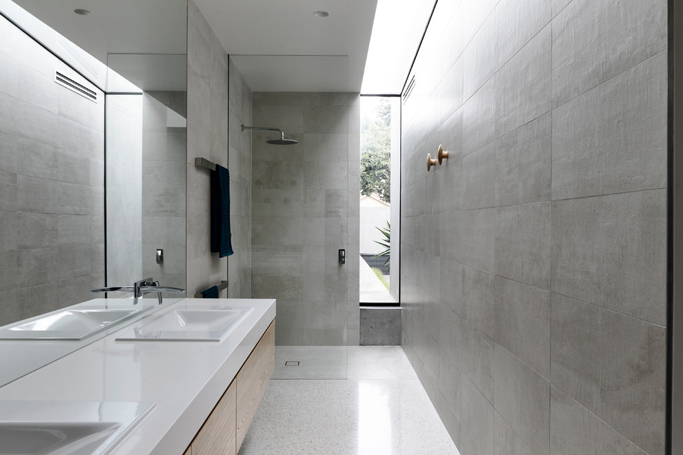 На фото: узкая и длинная ванная комната в стиле модернизм с плоскими фасадами, светлыми деревянными фасадами, душем без бортиков, серой плиткой, серыми стенами, душевой кабиной, накладной раковиной, белым полом и открытым душем