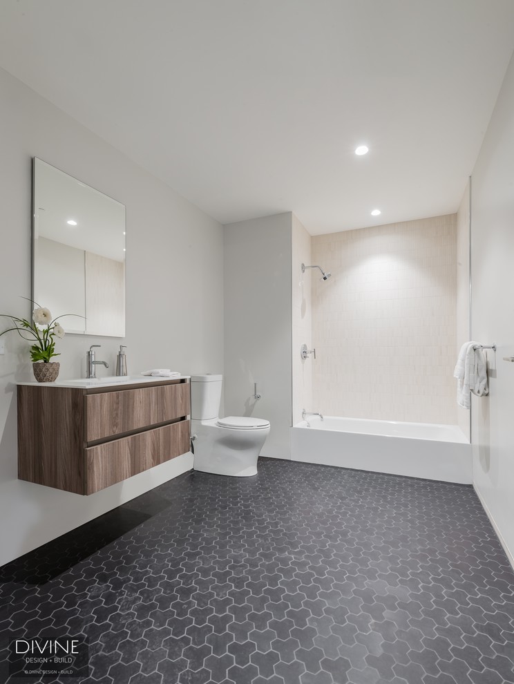 Example of a large trendy 3/4 gray tile and ceramic tile ceramic tile and gray floor bathroom design in Boston with flat-panel cabinets, light wood cabinets, a two-piece toilet, gray walls, an integrated sink and quartz countertops