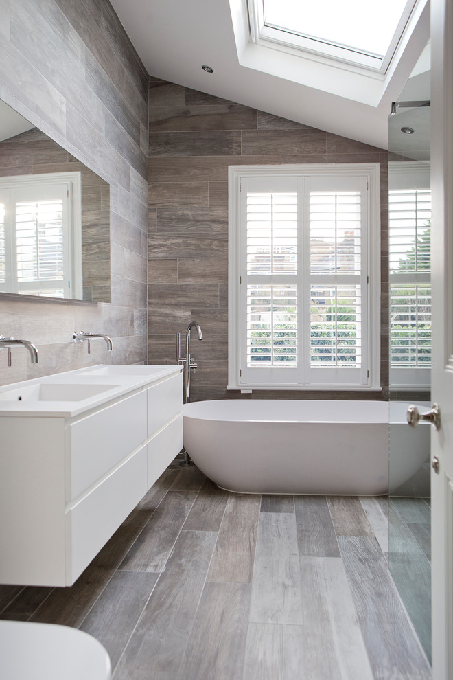 Exempel på ett modernt badrum med dusch, med släta luckor, vita skåp, ett fristående badkar, grå kakel, grå väggar, mellanmörkt trägolv, ett integrerad handfat och grått golv