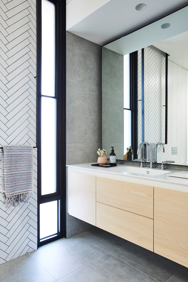 Diseño de cuarto de baño minimalista con armarios con paneles lisos, puertas de armario de madera clara, baldosas y/o azulejos blancos, lavabo integrado, suelo gris y encimeras blancas