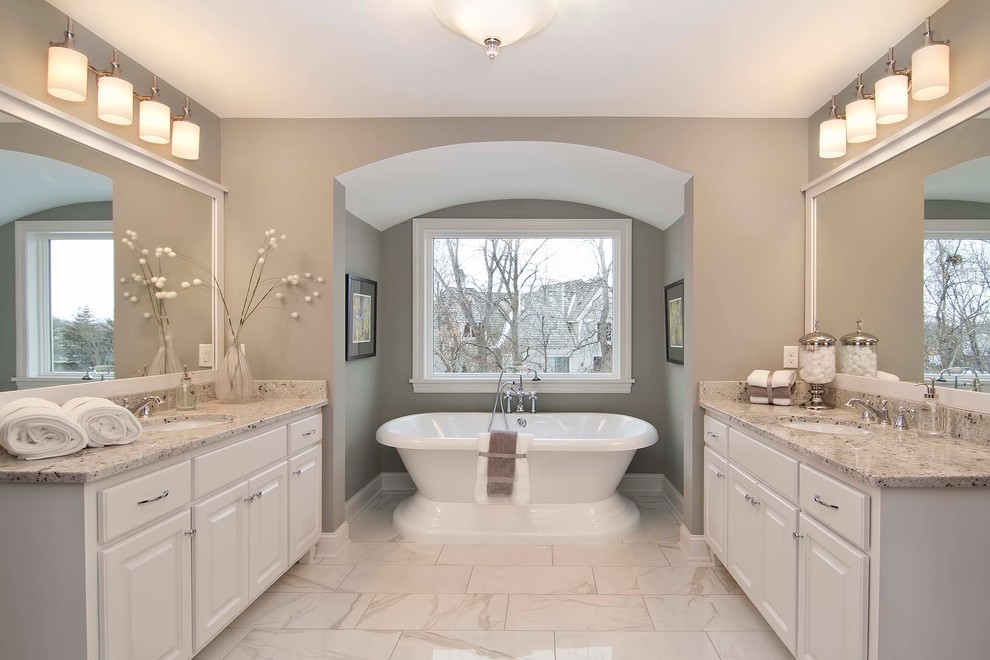 Diseño de cuarto de baño principal grande con lavabo encastrado, puertas de armario blancas, encimera de granito, bañera exenta y baldosas y/o azulejos blancos