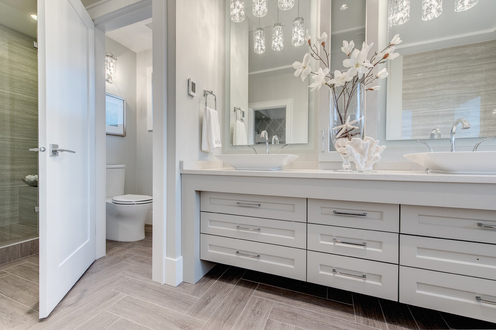 Medium sized traditional ensuite bathroom in Vancouver with recessed-panel cabinets, white cabinets, a one-piece toilet, grey walls, light hardwood flooring, a vessel sink, brown floors and grey tiles.