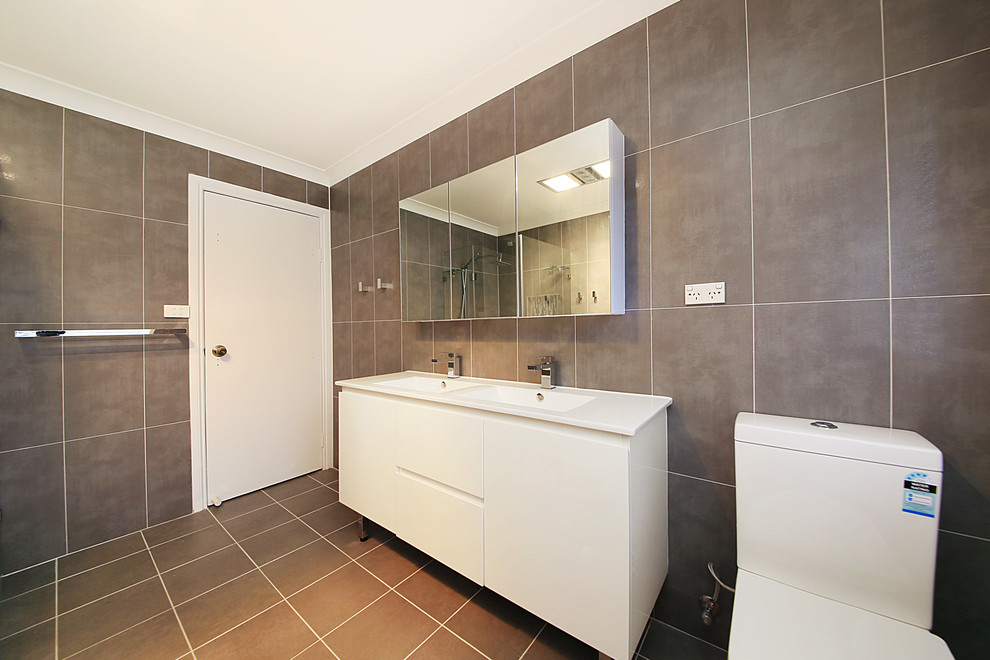 Modern inredning av ett stort en-suite badrum, med släta luckor, vita skåp, en toalettstol med separat cisternkåpa, brun kakel, bruna väggar, ett integrerad handfat och brunt golv
