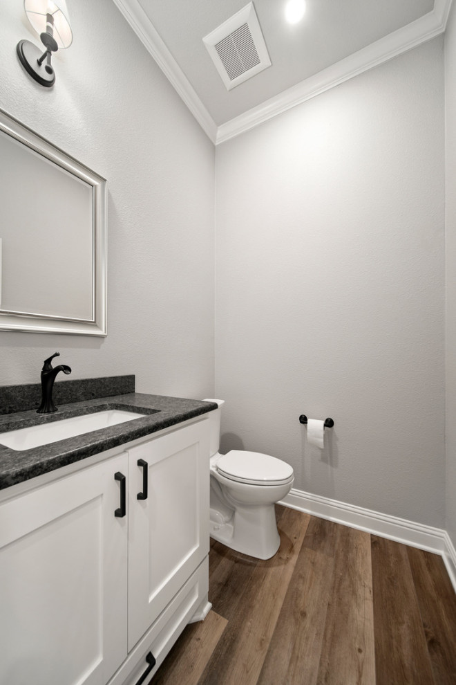 Réalisation d'un grand WC et toilettes tradition avec un placard à porte shaker, des portes de placard blanches, WC à poser, un mur gris, un sol en vinyl, un lavabo posé, un plan de toilette en granite, un sol marron, un plan de toilette noir et meuble-lavabo encastré.