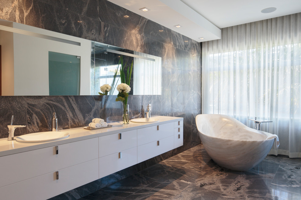 Стильный дизайн: главная ванная комната в современном стиле с плоскими фасадами, белыми фасадами, отдельно стоящей ванной, серой плиткой, накладной раковиной, серым полом и белой столешницей - последний тренд
