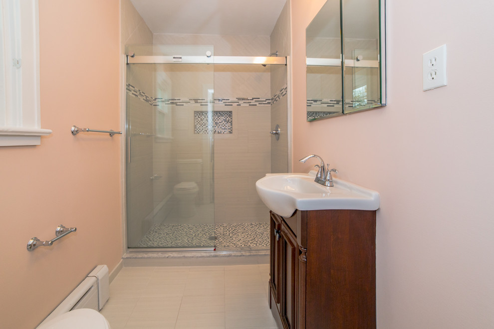 Example of a large transitional master gray tile and glass tile ceramic tile alcove shower design in Philadelphia with beaded inset cabinets, brown cabinets, a two-piece toilet, pink walls, a console sink and quartz countertops