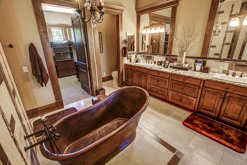 Photo of a large rustic ensuite bathroom in Boise with raised-panel cabinets, medium wood cabinets, a freestanding bath, a double shower, a one-piece toilet, beige tiles, travertine tiles, beige walls, travertine flooring, a built-in sink, granite worktops, beige floors, an open shower and multi-coloured worktops.