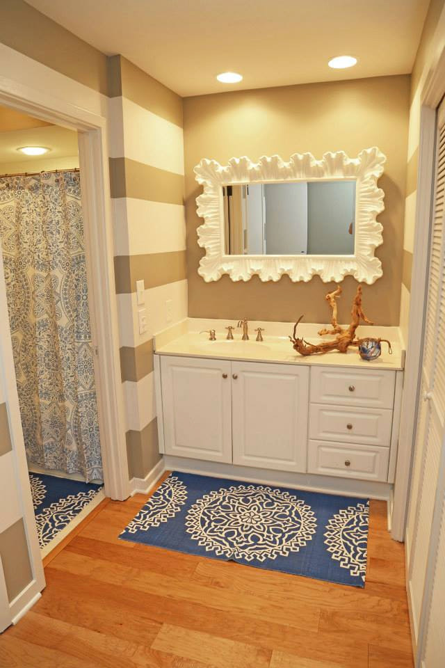 This is an example of a medium sized nautical ensuite bathroom in Other with raised-panel cabinets, white cabinets, an alcove bath, a shower/bath combination, a two-piece toilet, white tiles, ceramic tiles, beige walls, medium hardwood flooring, an integrated sink, solid surface worktops, brown floors, a shower curtain, white worktops, a single sink and a built in vanity unit.