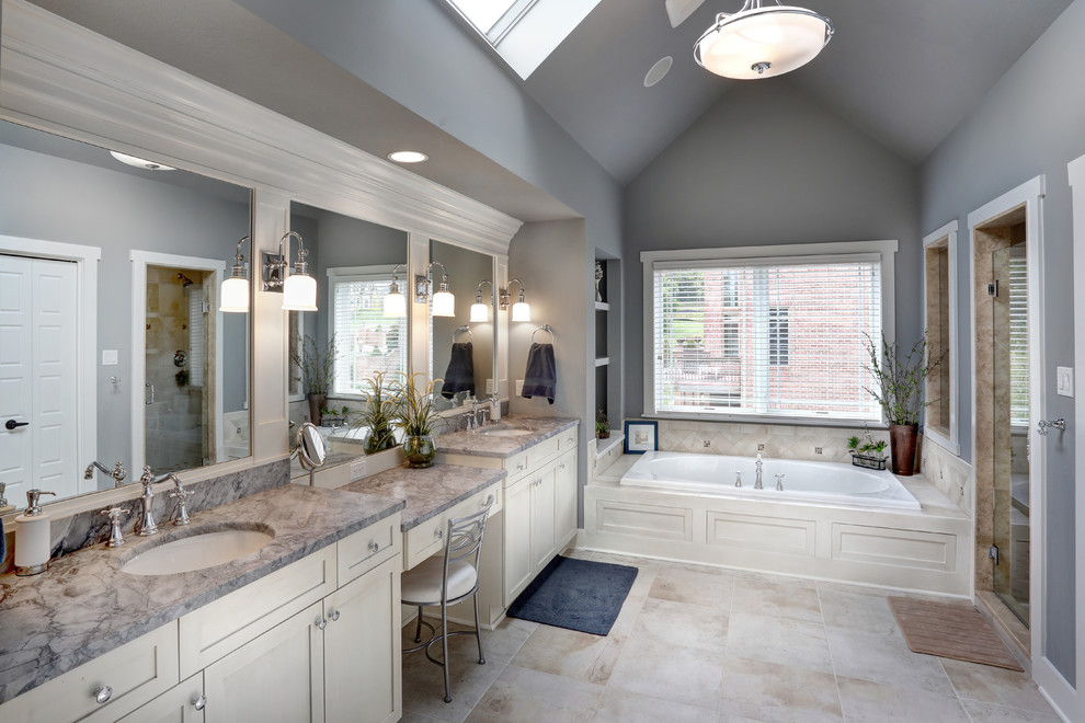 На фото: ванная комната в классическом стиле с врезной раковиной, фасадами в стиле шейкер, белыми фасадами, накладной ванной, душем в нише, бежевой плиткой, каменной плиткой и серыми стенами с