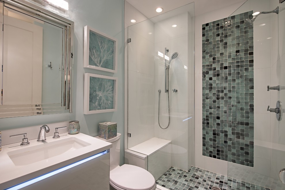 Maritim inredning av ett vit vitt badrum, med släta luckor, vita skåp, en dusch i en alkov, en toalettstol med hel cisternkåpa, flerfärgad kakel, blå väggar, ett undermonterad handfat och dusch med gångjärnsdörr