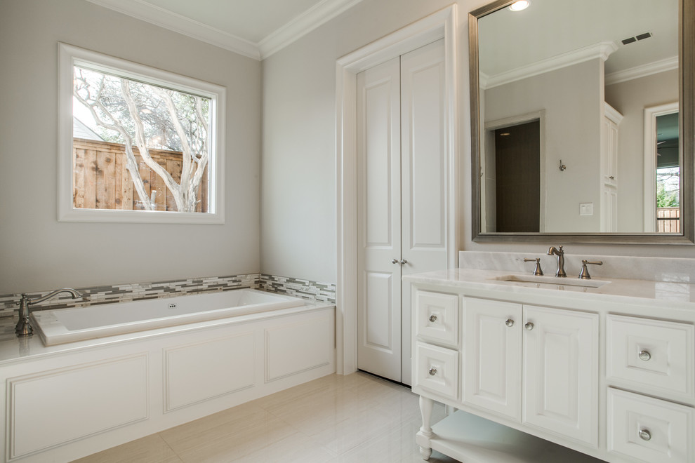 Ispirazione per una stanza da bagno padronale classica con consolle stile comò, ante bianche, top in marmo, vasca da incasso e piastrelle bianche